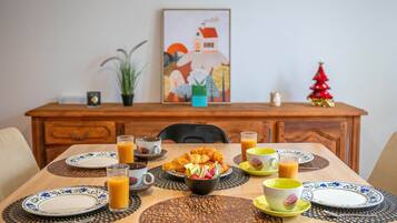 A dining table set with plates, cups, and a bowl of food, with a painting and a small Christmas tree on the wall behind.
