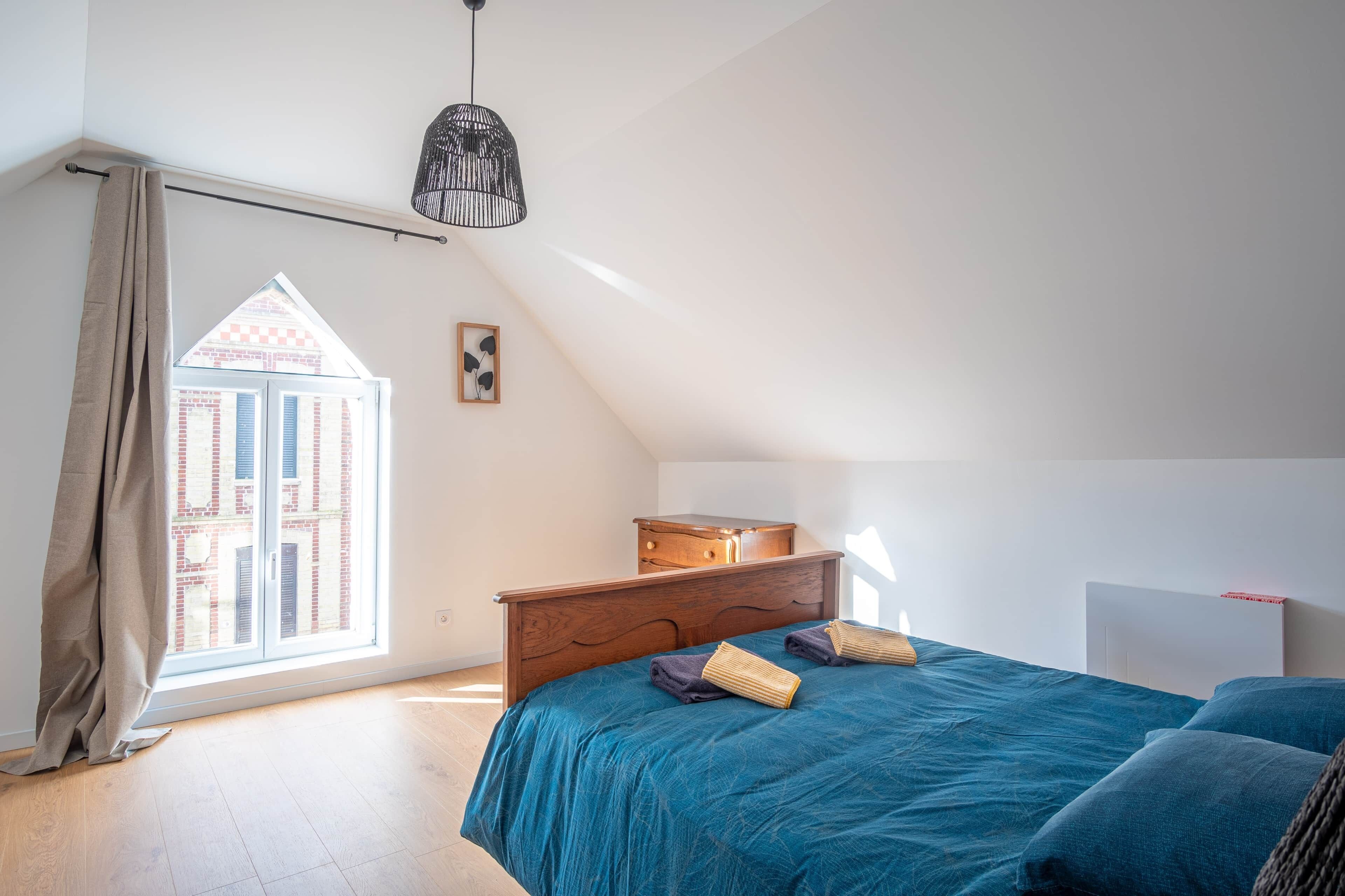 A bedroom with a large window, a bed, a dresser, and a radiator.