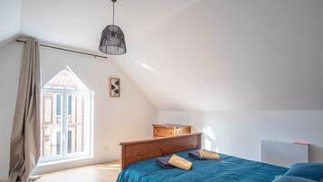 A bedroom with a large window, a bed, a dresser, and a radiator.