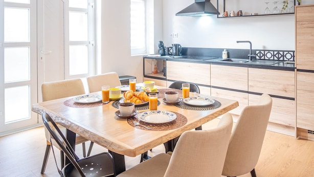 A modern kitchen with a dining table set for breakfast, featuring a coffee pot, croissants, and orange juice. - Gite le palefrenier - 6 pers - 10 min Etretat (Gonneville-la-Mallet)
