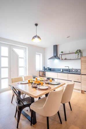 A modern kitchen with a dining table set for breakfast, featuring a coffee pot, croissants, and orange juice. - Gite le palefrenier - 6 pers - 10 min Etretat (Gonneville-la-Mallet)