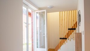 A modern interior with a wooden staircase, a glass door leading outside, and a light-colored floor. - Gite le palefrenier - 6 pers - 10 min Etretat (Gonneville-la-Mallet)