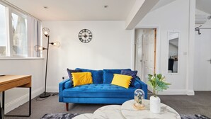 Ein modernes Wohnzimmer mit einem blauen Sofa, einem runden Couchtisch und einer Wanduhr.