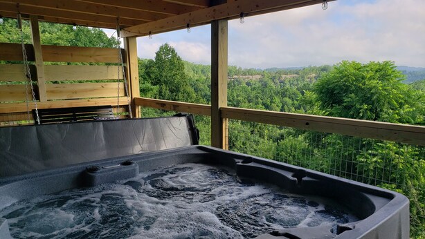 Una vasca idromassaggio con un pontile in legno e vista su un paesaggio verdeggiante.