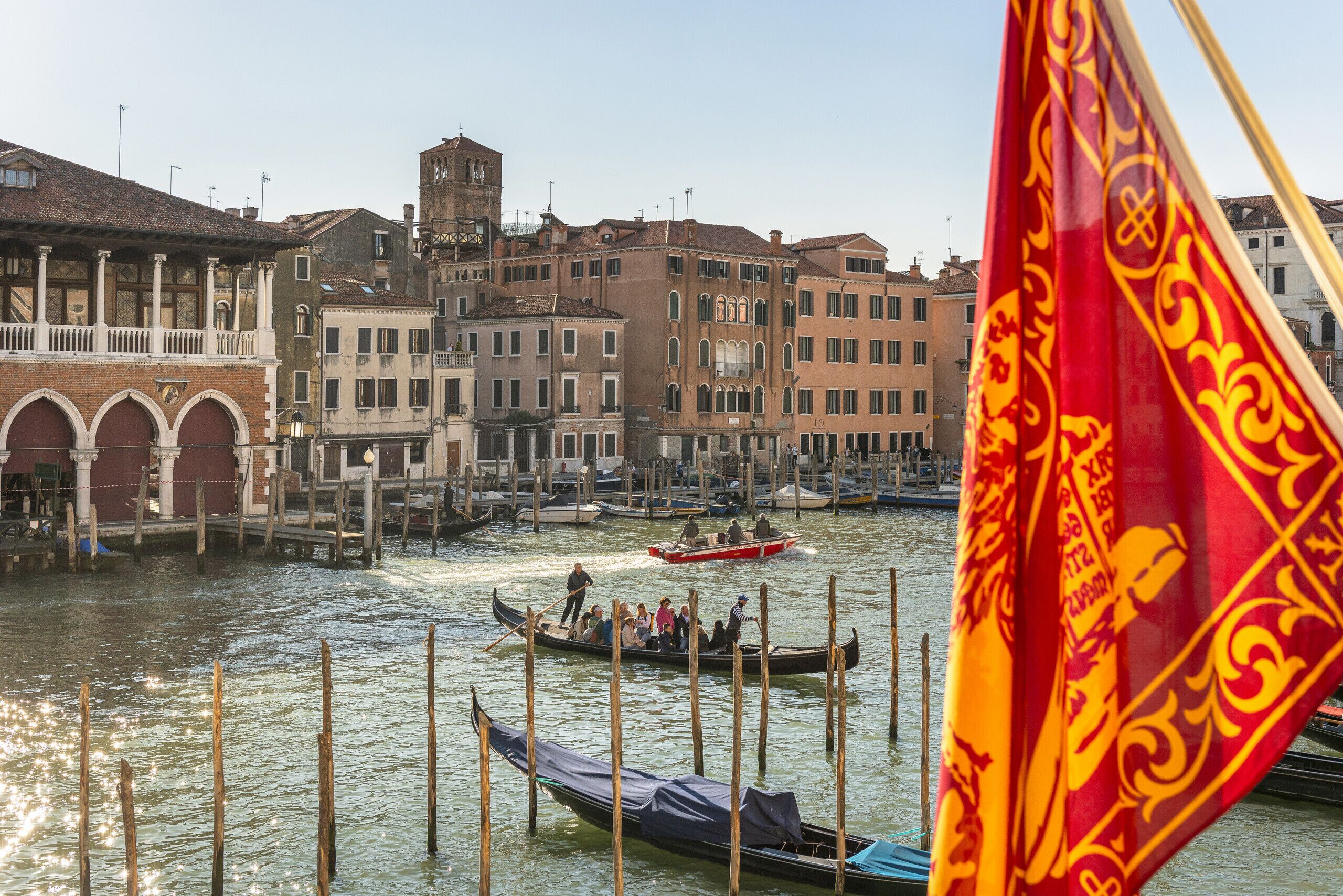 Un canal où l’on peut faire des promenades en gondole ou en bateau, des bâtiments historiques et un drapeau.