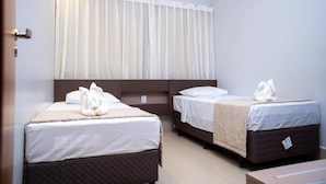 Ein Hotelzimmer mit zwei Betten, einem großen Fenster mit transparenten Vorhängen und einer Tür links.