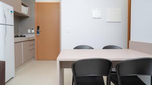 Eine kleine, moderne Küche mit Kühlschrank, Mikrowelle und einer Holztür. Ein Tisch mit vier Stühlen und eine Tafel an der Wand.