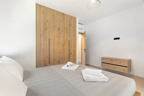 Un dormitorio moderno con una cama grande, un armario de madera, una mesita de noche y una lámpara colgante.