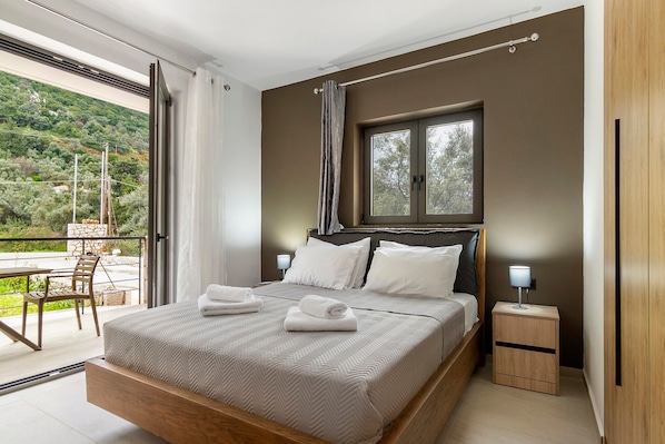 Un dormitorio con una cama grande, una ventana, una mesita de noche con lámpara y vistas a un balcón con mesa y sillas.