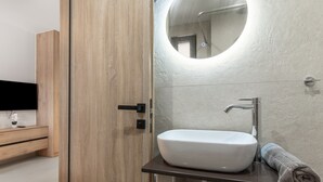 A bathroom with a wooden door, a white sink, a round mirror, and a towel. - Studio Apartment 'Sokol Stone House 2' with Mountain View, Wi-Fi and Air Conditioning (Ελλομένο)