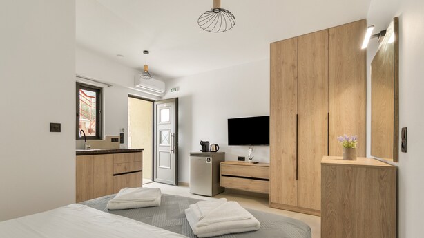 A modern hotel room with a bed, a TV, a wardrobe, and a kitchenette. - Studio Apartment 'Sokol Stone House 2' with Mountain View, Wi-Fi and Air Conditioning (Ελλομένο)