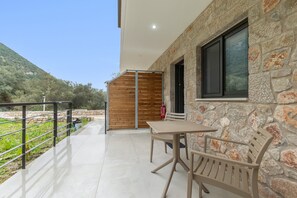 Un balcón con mesa y sillas, paredes de piedra y vistas a zonas verdes y colinas.