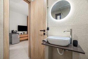 Un baño moderno con un lavamanos blanco, un espejo redondo y una puerta de madera.
