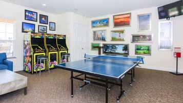 A room with a ping pong table, arcade games, and framed pictures on the walls.