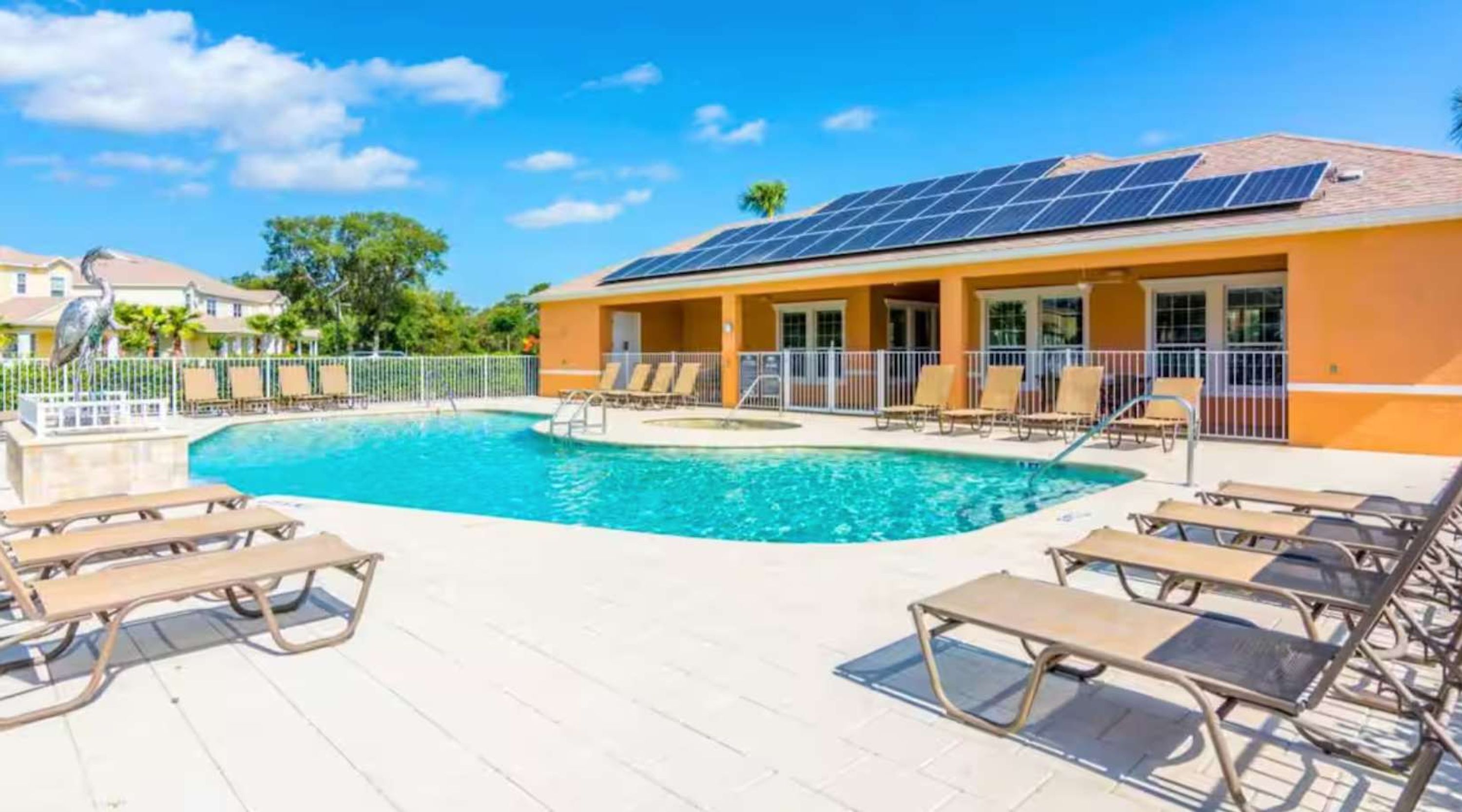 A swimming pool with lounge chairs, a building with solar panels, and a clear blue sky.