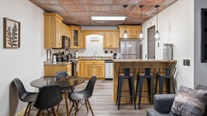 Eine moderne Küche mit Holzausbau, einer zentralen Kochinsel mit Barhocker und einem Essbereich mit rundem Tisch und Stühlen.
