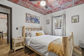 Quarto com cama de madeira, mesa de cabeceira, janela com cortinas e teto com padrão em vermelho e azul.