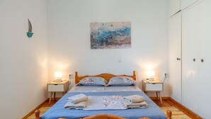 A bedroom with a wooden bed, two bedside tables with lamps, a wall-mounted artwork, and a wardrobe. - Holiday Home 'Hippocrates' with Mountain View, Wi-Fi and Air Conditioning (Amorgos)