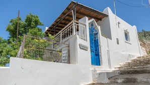 A white building with a blue door, a balcony, and a staircase leading up to the entrance. - Holiday Home 'Hippocrates' with Mountain View, Wi-Fi and Air Conditioning (Amorgos)
