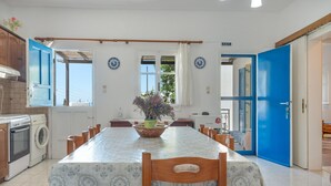 A dining area with a table set for six, a washing machine, and a blue door. - Holiday Home 'Hippocrates' with Mountain View, Wi-Fi and Air Conditioning (Amorgos)