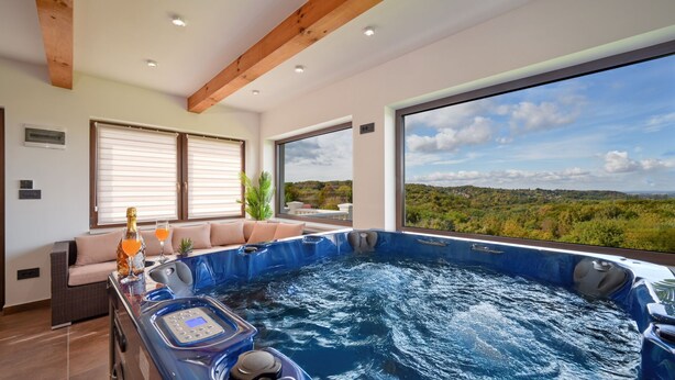 A modern spa room with a hot tub, a control panel, and a view of the landscape.