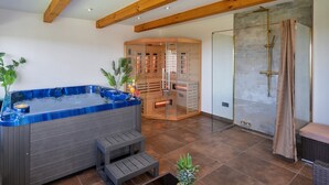 A hot tub, a glass-enclosed sauna, and a shower area in a modern bathroom.