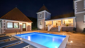 A swimming pool with lounge chairs, a staircase leading to a covered porch, and a two-story building with a dormer window.