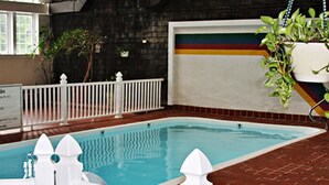 An indoor swimming pool with a white fence, a brick floor, and a wall with a colorful stripe. - Crafts Inn, Hotel Suite with pool and hot tub. (Wilmington)