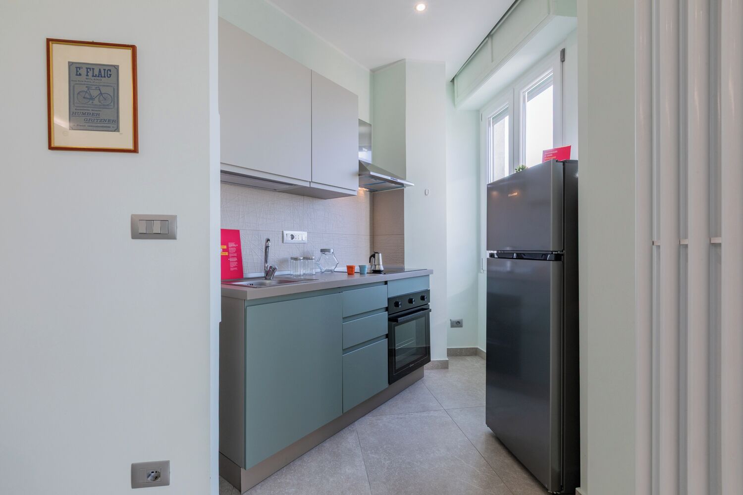 A modern kitchen with light blue cabinets, a stainless steel refrigerator, and a built-in oven.