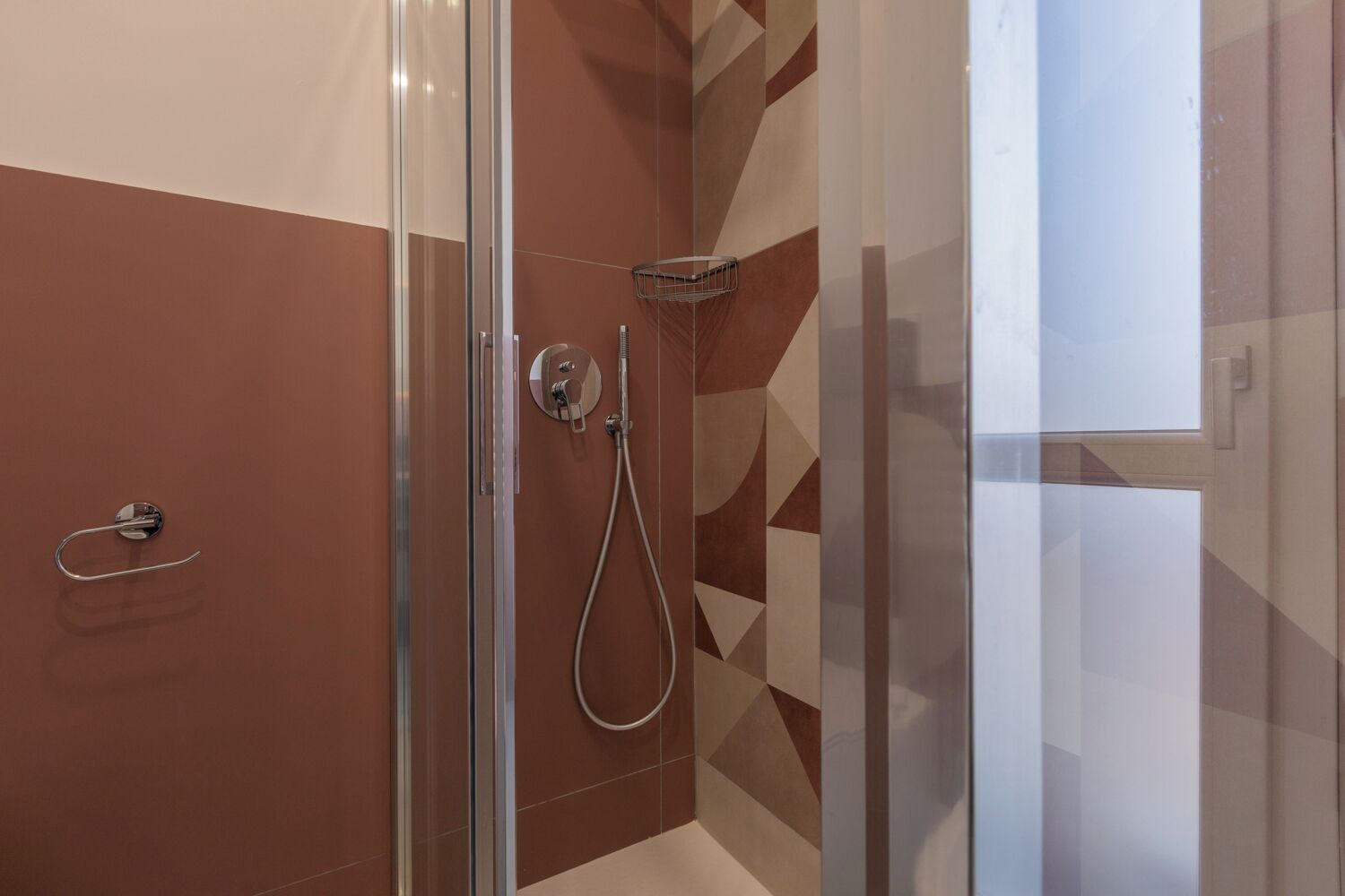 A glass-enclosed shower with a handheld showerhead and a wall-mounted faucet.