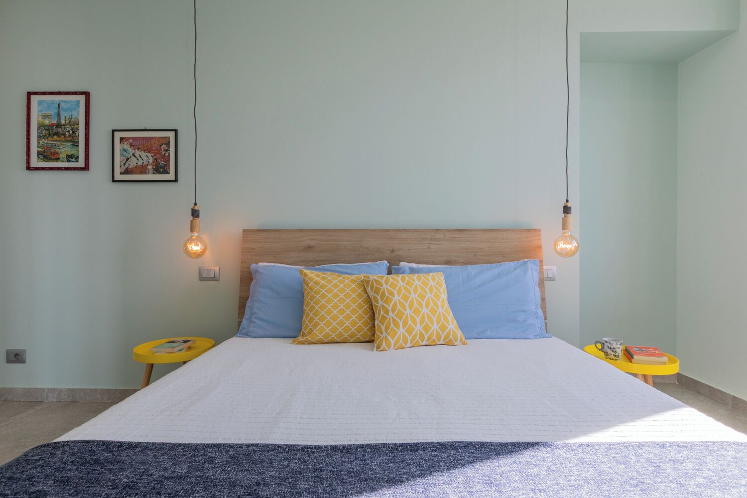 A bedroom with a large bed, two bedside tables, and two wall-mounted light fixtures.