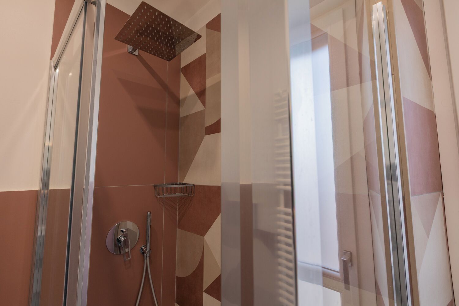 Un'area doccia moderna con porta in vetro, soffione a mano e soffione a pioggia montato a parete.