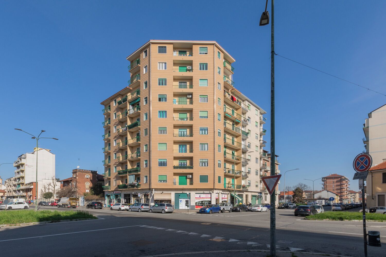 A multi-story residential building with balconies, a pedestrian crossing, and a no parking sign.