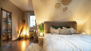 Une chambre avec un grand lit, une table de chevet avec une lampe, une fenêtre avec des rideaux et une vue sur l’extérieur.