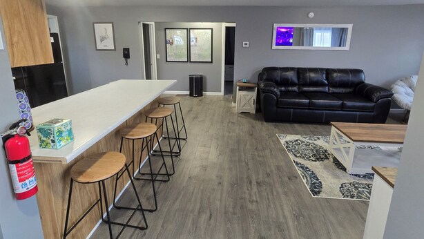 A modern kitchen with a white countertop and bar stools, a black leather sofa, and a patterned rug. - Charming 3-bedroom house in Presque Isle (Presque Isle)