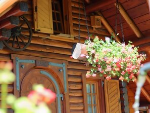 A wooden cabin with a large arched door, a hanging flower basket, and a wooden wheel.