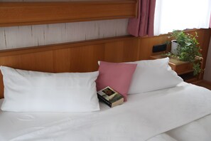 A neatly made bed with white and pink pillows, a bedside table with a book and a plant, and a wooden headboard.