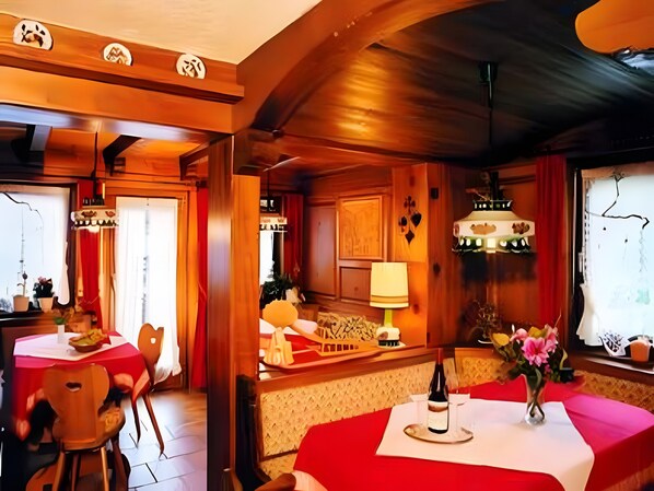A restaurant with wooden interiors, red tablecloths, and a wine bottle on the table.