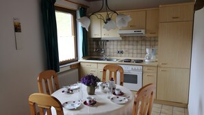 Un comedor con una mesa redonda dispuesta para cuatro personas, una cocina con armarios de madera, estufa y cafetera.
