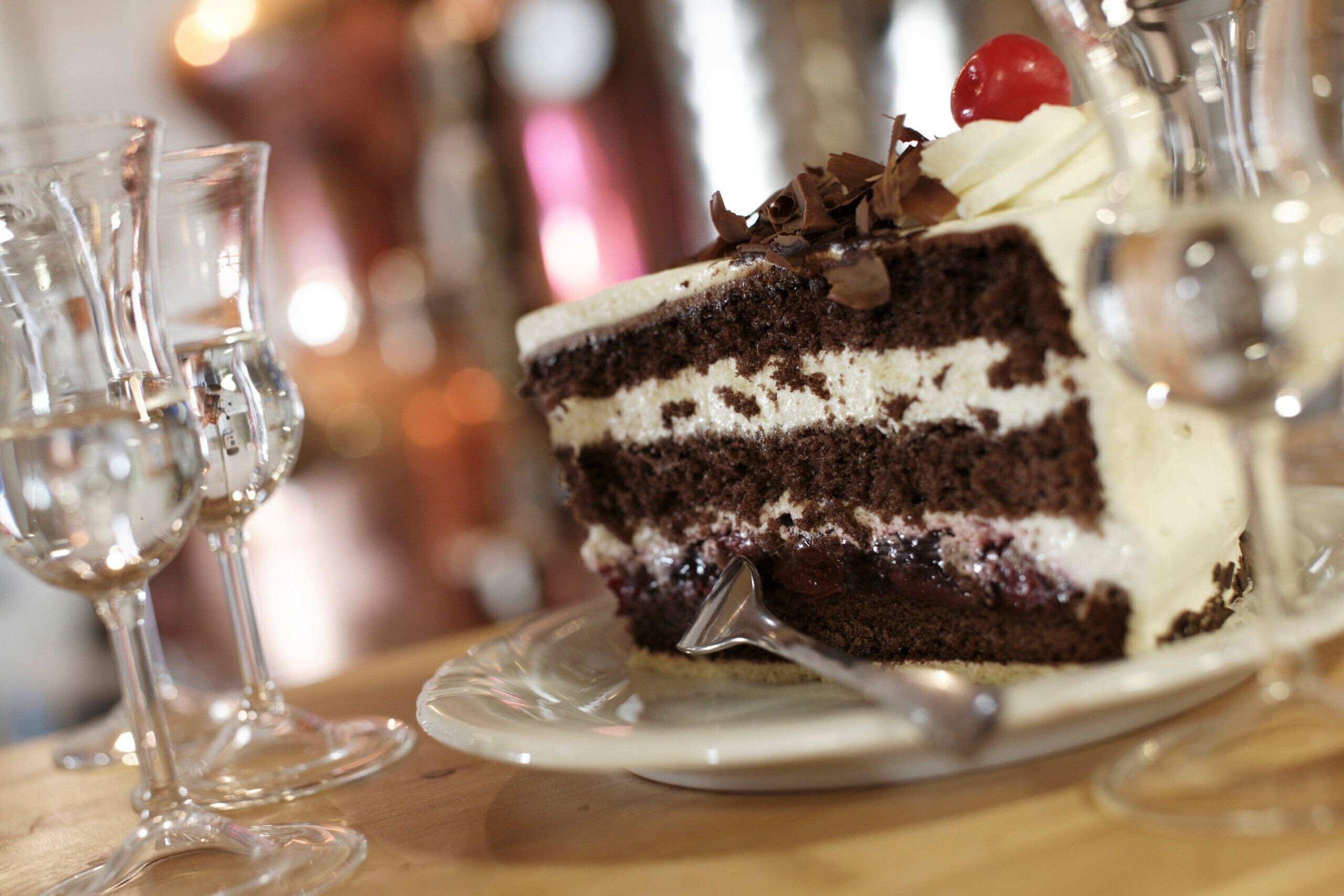 A slice of layered chocolate cake with whipped cream and a cherry on a glass plate.