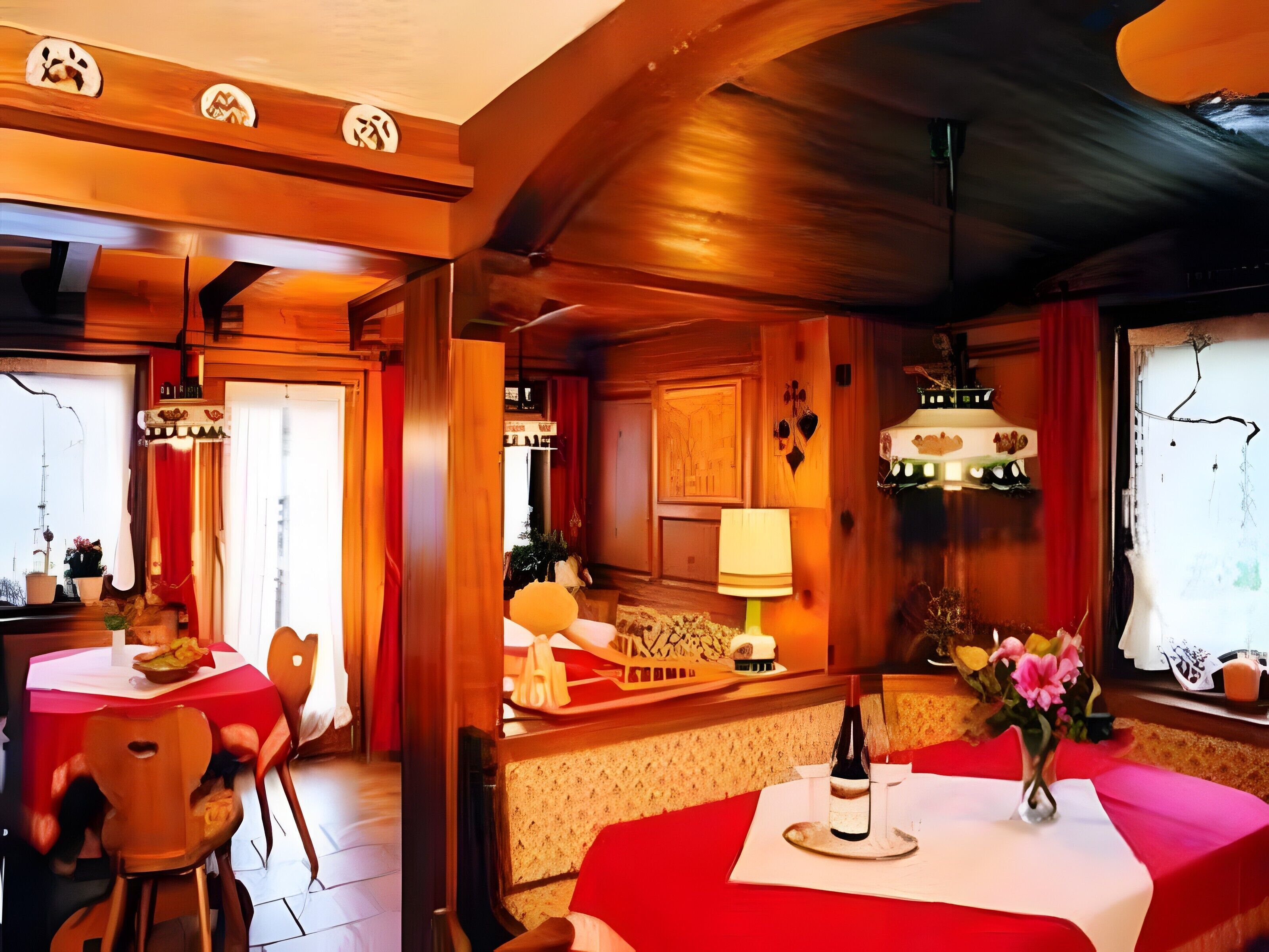 A restaurant with wooden interiors, red tablecloths, and a wine bottle on the table.
