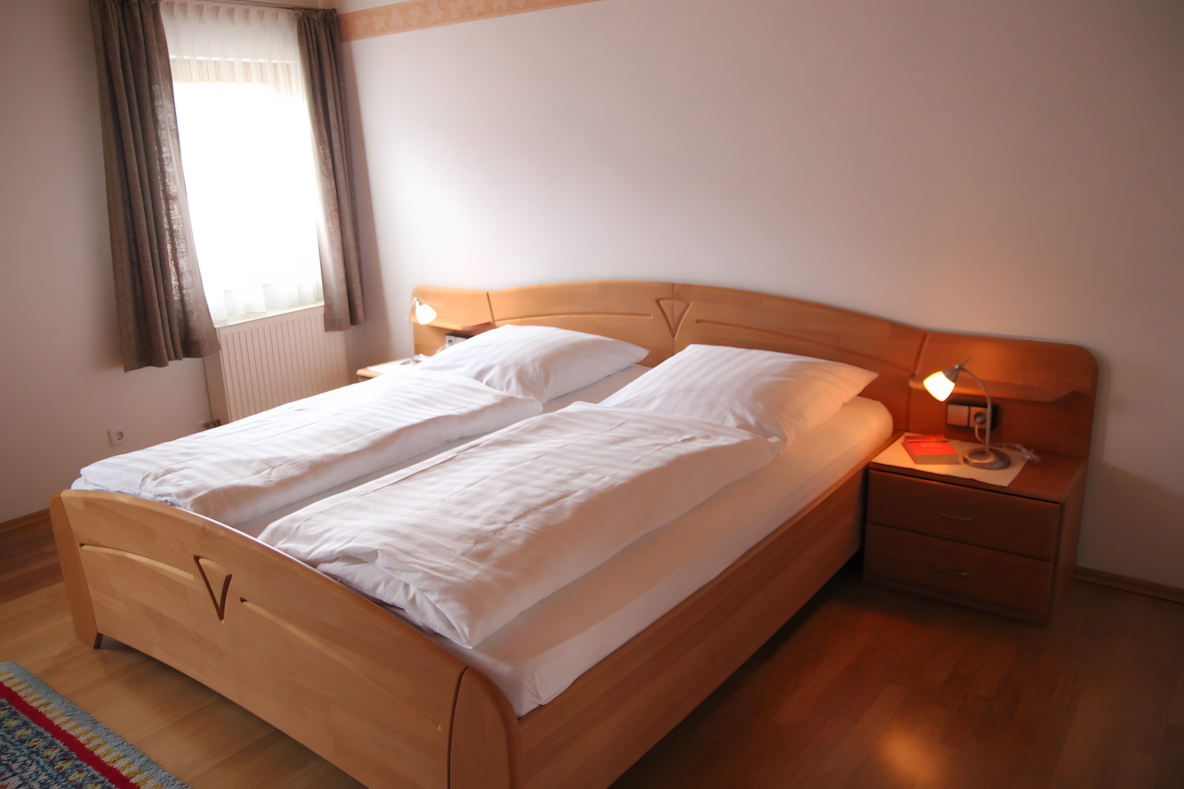 A double bed with a wooden headboard, a bedside table with a lamp, and a window with curtains.
