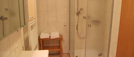 A bathroom with a glass-enclosed shower, a wooden bench, and a white sink.