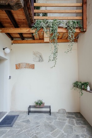 A stone-floored interior with a wooden ceiling, a bench, and hanging plants.