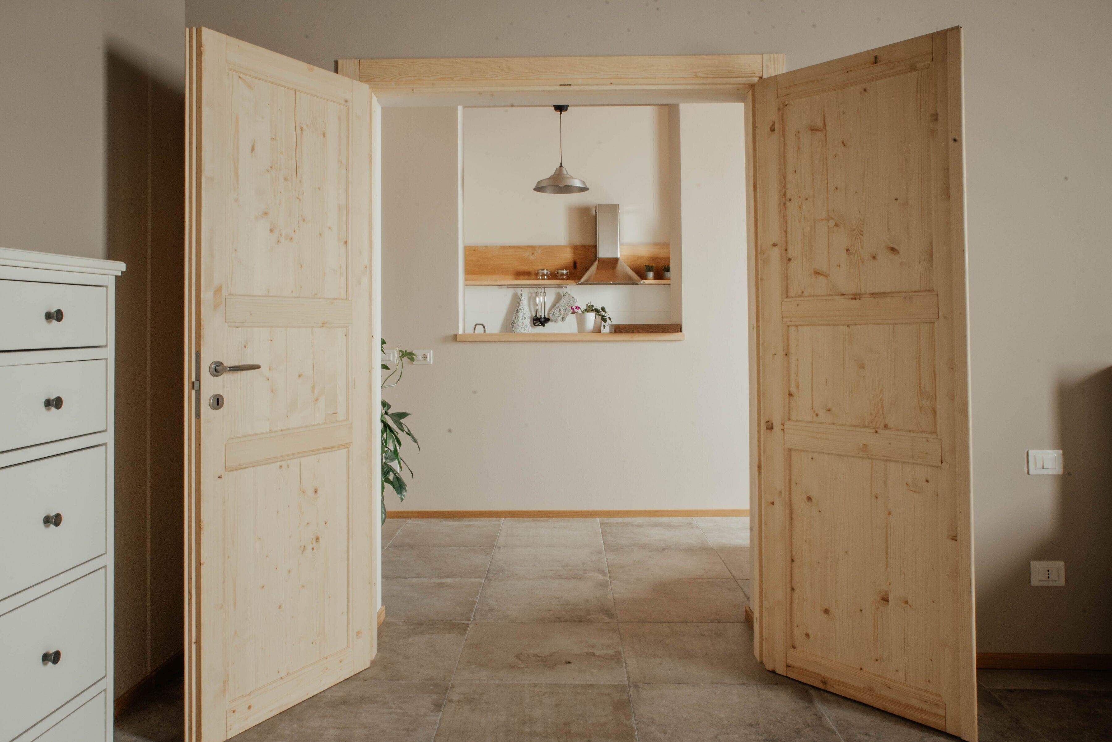 A room with a wooden door, a white dresser, a hanging light fixture, and a tiled floor.