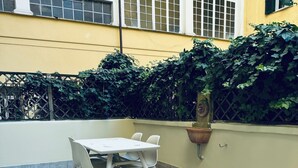 A small outdoor patio with a table and chairs, a potted plant, and a wall with a lattice fence and greenery.