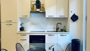 A modern kitchen with white cabinets, a black countertop, and a glass dining table with four chairs.