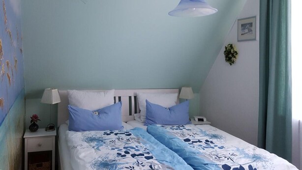 A bedroom with a bed, bedside tables, a lamp, and a hanging light fixture. - Ferienwohnung in St. Peter-Ording (St. Peter-Ording)