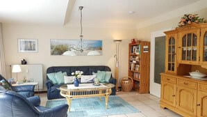 A living room with a sofa, a coffee table, a bookshelf, and a cabinet. - Ferienwohnung in St. Peter-Ording (St. Peter-Ording)