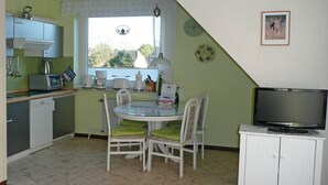 A compact kitchen with a dining table, chairs, a television, and a window with a view of the outside. - Ferienwohnung in St. Peter-Ording (St. Peter-Ording)
